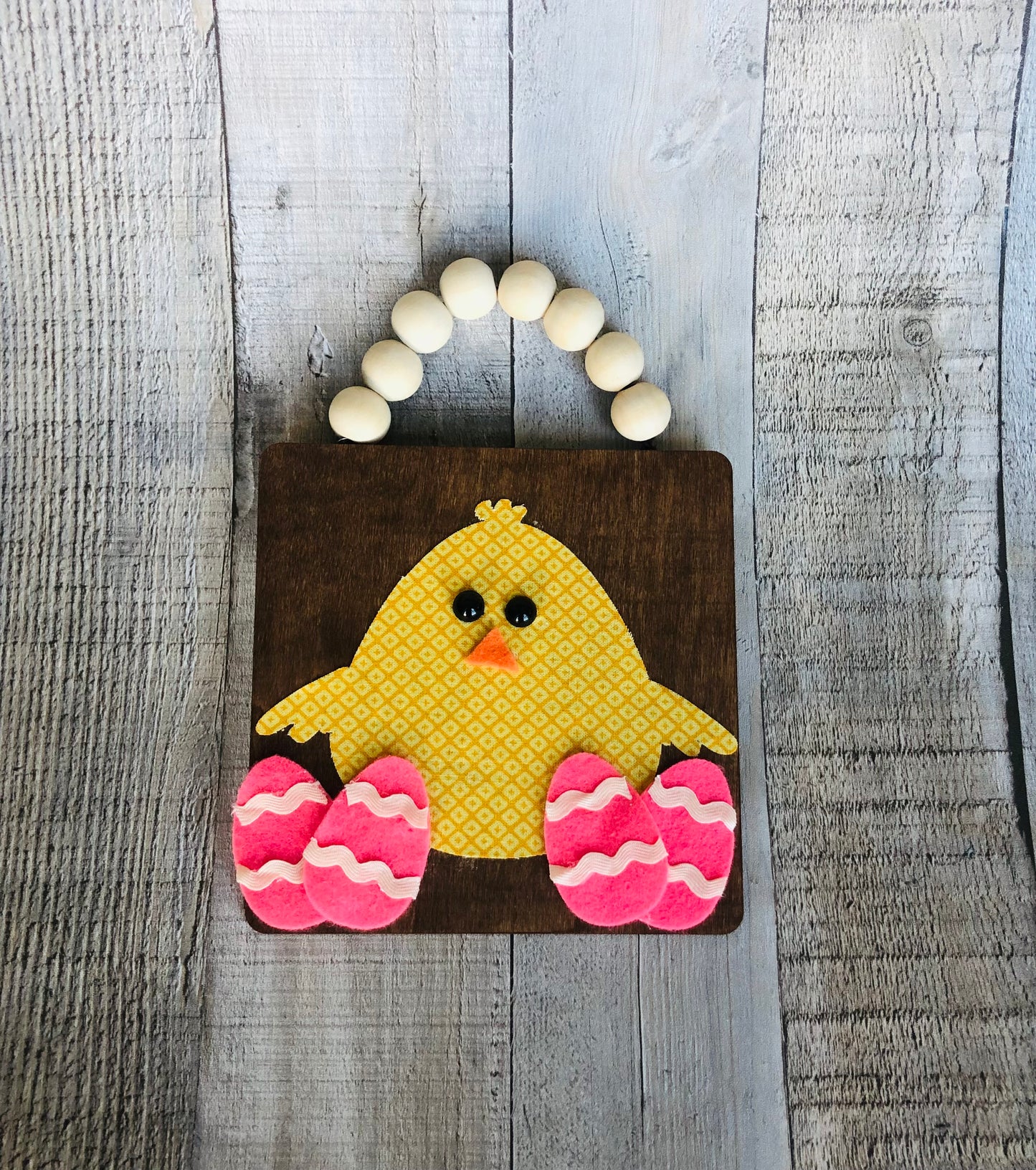 This is an Easter craft of a chick with Easter eggs on a wooden plaque with a wood bead handle.
